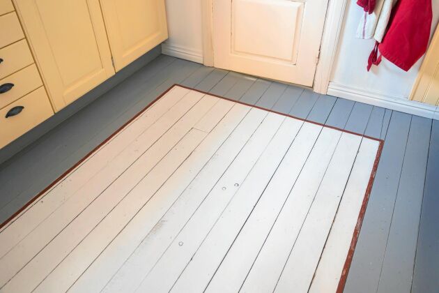 De grå golvplankorna har målats med röda ramar både i hallen och arbetsköket så att det ser ut som att det ligger mattor på golvet. 